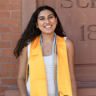 Image of female student with gold graduation drape standing in front of Old Main brick wall.